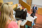 Rear view of a female using laptop with students and teacher at the college lecture hall