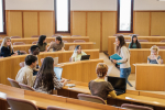 Group of university students in a circular classroom with the teacher in the middle explaining