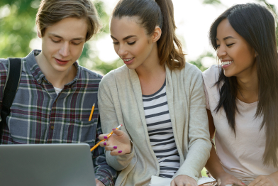 Multiethnic group of young smiling students using laptop computer