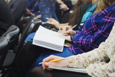 Spectators at seminar — students or businessmen at a conference or presentation, workshop, master class — pens and notebooks in hand, close up