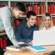 University students sitting together at table with books and laptop. Happy young people doing group study in library