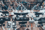 Young and successful. Top view of group of young business people in smart casual wear working together and smiling while sitting at the large office desk